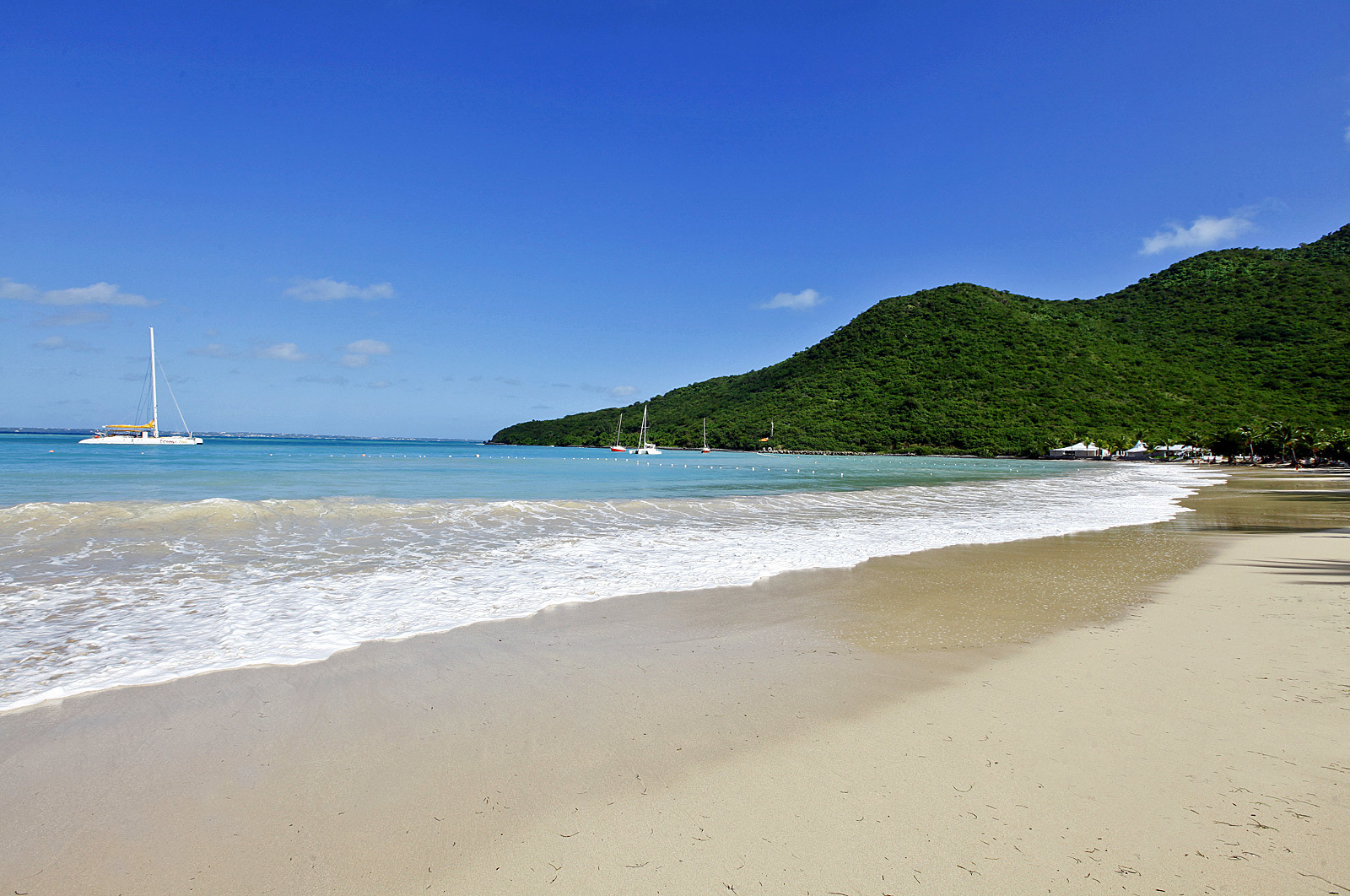 Strand med segelbåt och berg i bakgrunden