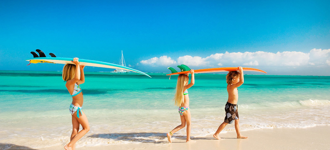 Tre barn som bär surfbrädor på stranden
